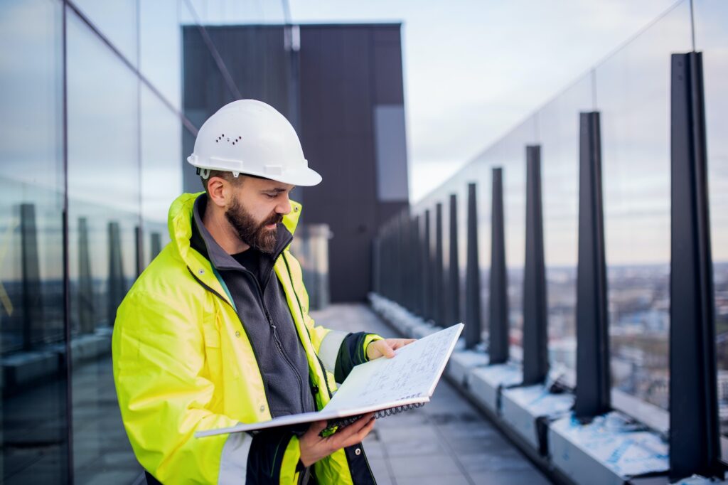 Man engineer standing on construction site, holding blueprints. Professional Drywall & Finishing Services in Waterloo | Off Plan Contractor Inc.